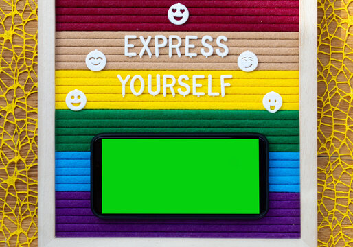 Words EXPRESS  YOURSELF with red bow on rainbow surface. Smart phone with green screen. Closeup.