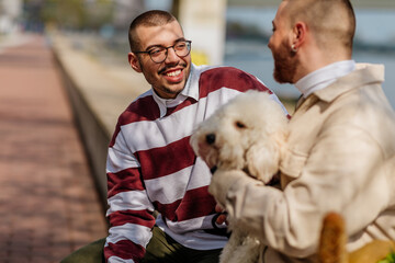Gay couple sitting on quay with dog and enjoying sunny day