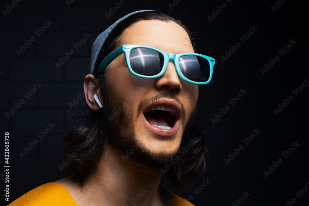 Wall mural studio portrait of young man with wireless earphones wearing blue sunglasses on black background.