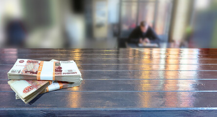 Russian five-thousand-dollar bills on a dark wooden table. Five million rubles in a bank sticker. A wad of money.