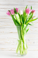 Fresh spring tulips in glass vase on white wooden background close up.