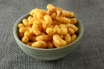 Peanut buttery corn puff snack in ceramic bowl on grey burlap
