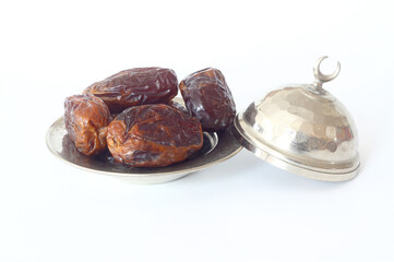 Dried palm date fruits in a silver bowl on white background.