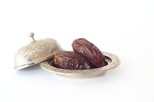 Dried palm date fruits in a silver bowl on white background.