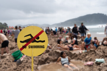 No Swimming Sign at Hotwater Beach, with crowds of people, Coromandel New Zealand, selective focus