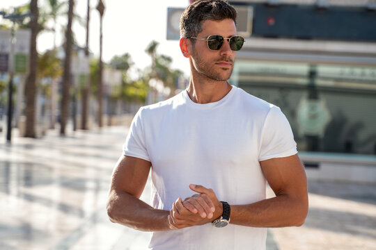 Portrait of handsome young man wearing sunglasses and white tshirt, posing on city street background. Casual style. - Powered by Adobe