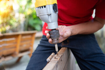A man is using a drill to fix a steel hinge on a wooden door to repair the damage in the house.