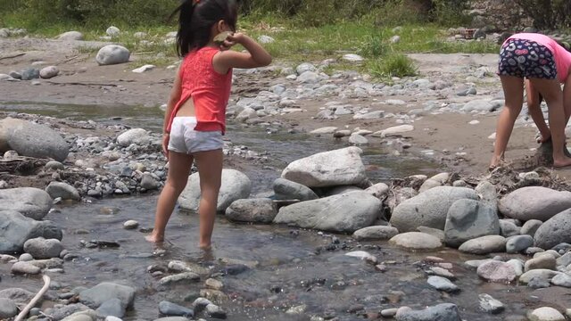 slow motion of a little girl throwing rocks in a river near her sister on a family vacation trip close to the city during the day