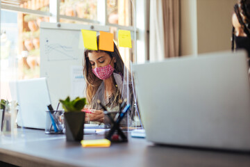 Business women wearing protective masks sitting at their desks separated by plexiglass dividers