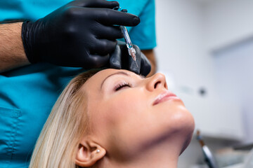 Obraz na płótnie Canvas Attractive young woman is getting a rejuvenating injections. She is sitting calmly at clinic. The expert beautician is filling female lips by hyaluronic acid.