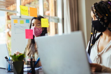 Business women wearing protective masks sitting at their desks separated by plexiglass dividers