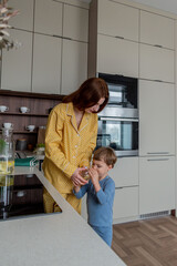 Young mother pours water a glass. Kitchen little boy is drinking.