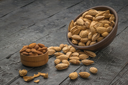 A small cup with peeled almonds and a large clay bowl with unpeeled almonds spilling out.