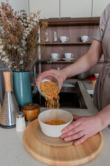 Senior woman pours cereals from plastic container into glass jar.
