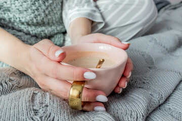 Young woman sits on a bed in the bedroom and drinks hot coffee. Defocus.