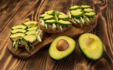 Healthy vegetarian organic breakfast meal, sandwich food made from asparagus, avocado, cucumber, soft cheese on whole grain buns. Wooden board, close up