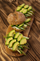 Healthy vegetarian organic breakfast meal, sandwich food made from asparagus, avocado, cucumber, soft cheese on whole grain buns. Wooden board, close up