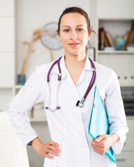 Woman doctor wear white medical uniform and stethoscope with blue folder of documents in clinic