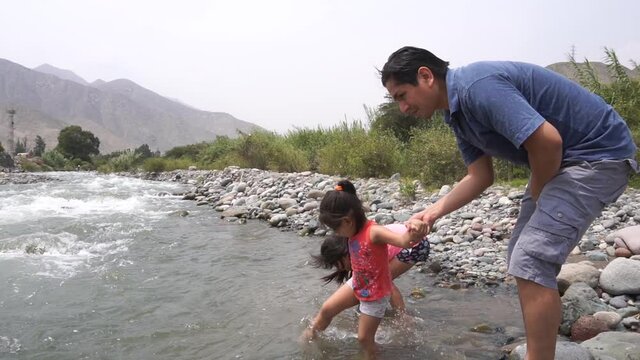 slow motion of a dad and his two little daughters playing in a river on a family vacation trip during the day