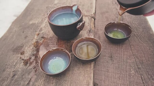 Man hand pours green Chinese tea gaba oolong into clay cups which stand on mahogany planks. Drink exudes a strong steam and aroma. Concept of traditional Oriental tea drinking and healthy lifestyle