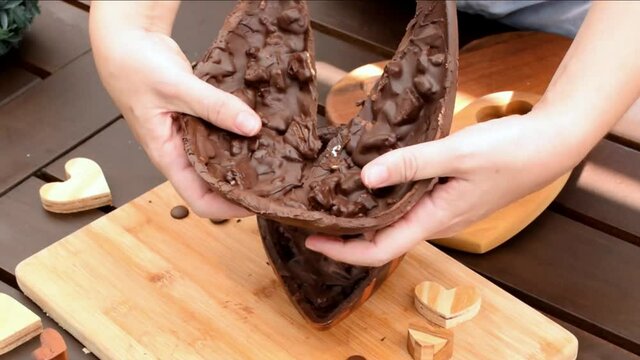 Woman breaking and showing half of a dark chocolate Easter egg with crispy almond. Zoom in anda slow motion.