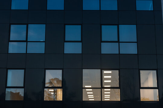 Facade of a business district building, a high rise, at night, in the evening, with only a few windows lit, for employees  working late in this office building