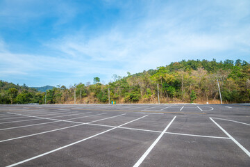 Empty space outdoor asphalt parking lot in national park. Large car park with white line paint on mountain hill in sunny day blue sky background.