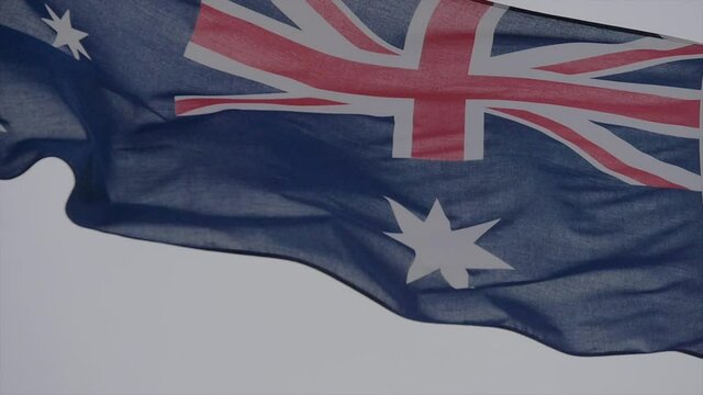 The Australian flag waving in a strong wind against a grey sky background. National pride and patriotic themed concept.