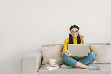 Young attractive woman student study online with laptop, sitting on sofa at home. Distance learning and remote teaching concept with empty text place.