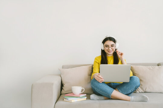Young attractive woman student study online with laptop, sitting on sofa at home. Distance learning and remote teaching concept with empty text place.