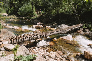 Wooden bridge over a small mountain river in a spring forest. Sunny afternoon.
