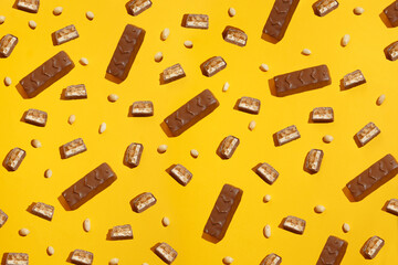 Pieces chocolate bar on a background of peanuts. Modern composition on yellow background