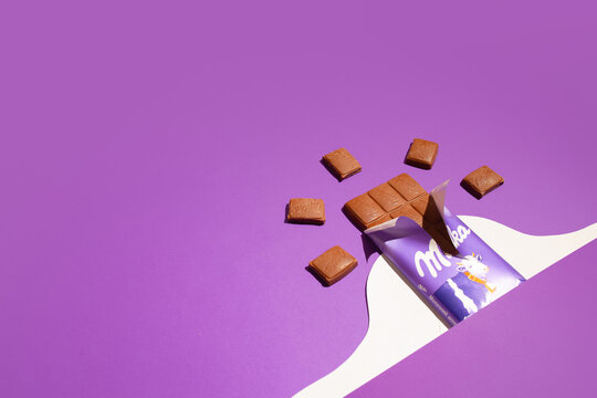 Kiev, Ukraine - April 4, 2021: Milka chocolate in an open package and pieces of a bar on a purple background. Modern composition