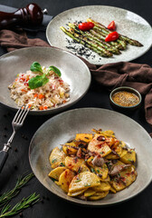 Dinner plates on dark background. Homemade fried potatoes with mushrooms, grilled asparagus and basmati rice with vegetables. Vegetarian and healthy food concept, clean eating, close up