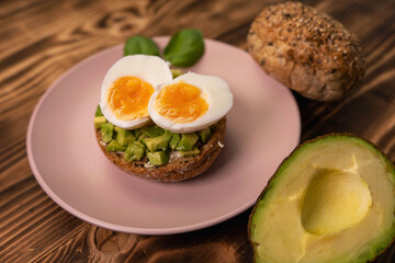 Healthy vegetarian food breakfast meal, sandwich made from avocado cubes with sunflower oil, soft cheese, cucumber and boiled egg on whole grain buns. Wooden board, close up