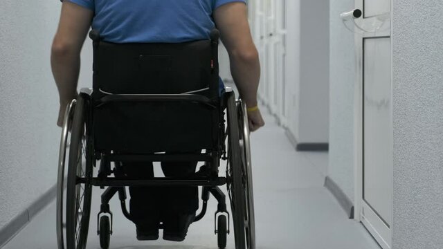 A man in a wheelchair drives down the hallway. A person with a disability moves around the hospital.
