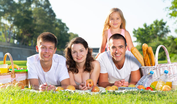 Cheerful parents with two child laying in summer grass plant on the picnic. High quality photo