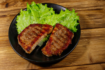 Grilled pork steaks with lettuce leaves on wooden table