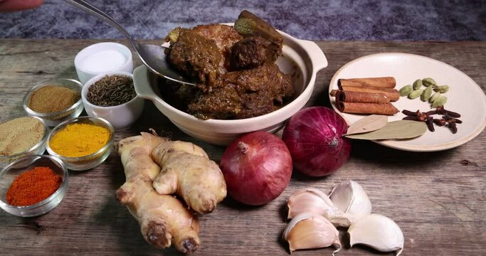 Beef bhuna dry curry with potato in ceramic bowl ingredients chilli cumin coriander turmeric powered salt onion garlic ginger bay leaf cinnamon cardamom clove over rustic wood background