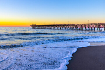 Wooden fishing pier sunrise on the ocean in Myrtle Beach, South Carolina, USA.