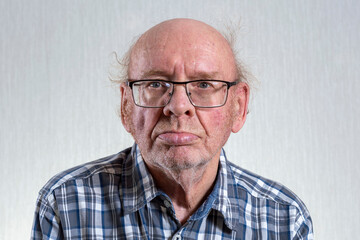 Old unshaven bald man with glasses. Indoors in daylight. Front view.