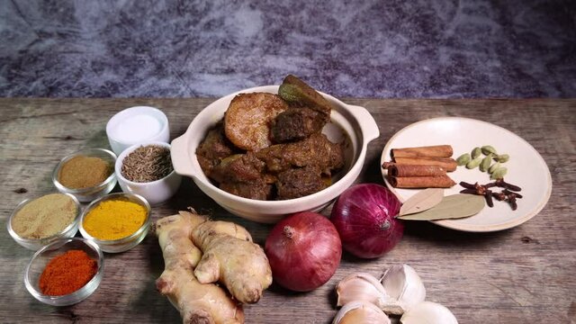 Beef bhuna dry curry with potato in ceramic bowl ingredients chilli cumin coriander turmeric powered salt onion garlic ginger bay leaf cinnamon cardamom clove over rustic wood background 
