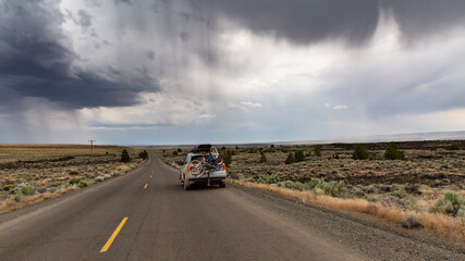 Diamond Craters Loop, Oregon / USA - 23 July 2020: Honda Pilot with mounted Yakima roof box and bikes on a bike rack on the road in the middle of a desert landscape against gloomy rainy sky.