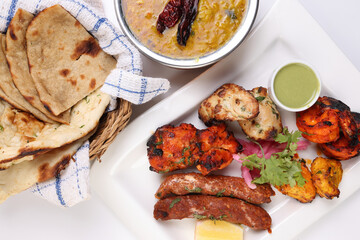 Mixed grill kebab chicken mutton beef prawn fish mint sauce lemon pickled onion bread basket chapati naan tandoori paratha dal lentil fry tadka copper pot on white dish over white background