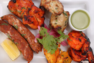 Mixed grill kebab chicken mutton beef prawn fish mint sauce lemon pickled onion coriander on white dish over white background