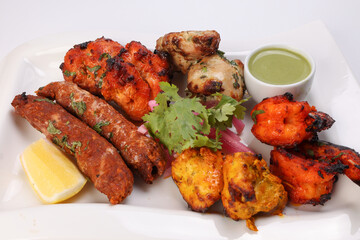 Mixed grill kebab chicken mutton beef prawn fish mint sauce lemon pickled onion coriander on white dish over white background