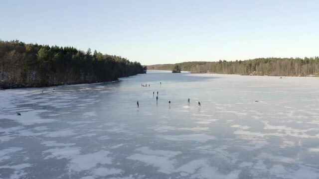 An aerial drone shot of a group of people ice skating on a large frozen lake - Daytime.