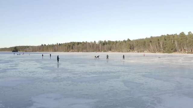 A group of people playing ice hockey on a large frozen lake surrounded by tall green trees.