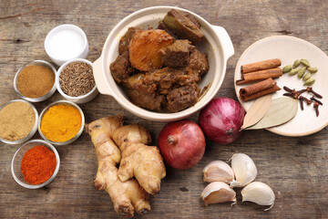 Beef bhuna dry curry with potato in ceramic bowl ingredients chilli cumin coriander turmeric powered salt onion garlic ginger bay leaf cinnamon cardamom clove over rustic wood background