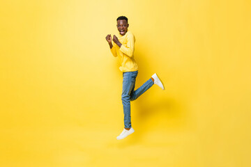 Young cheerful excited African man jumping with clenching hands on isolated yellow studio background